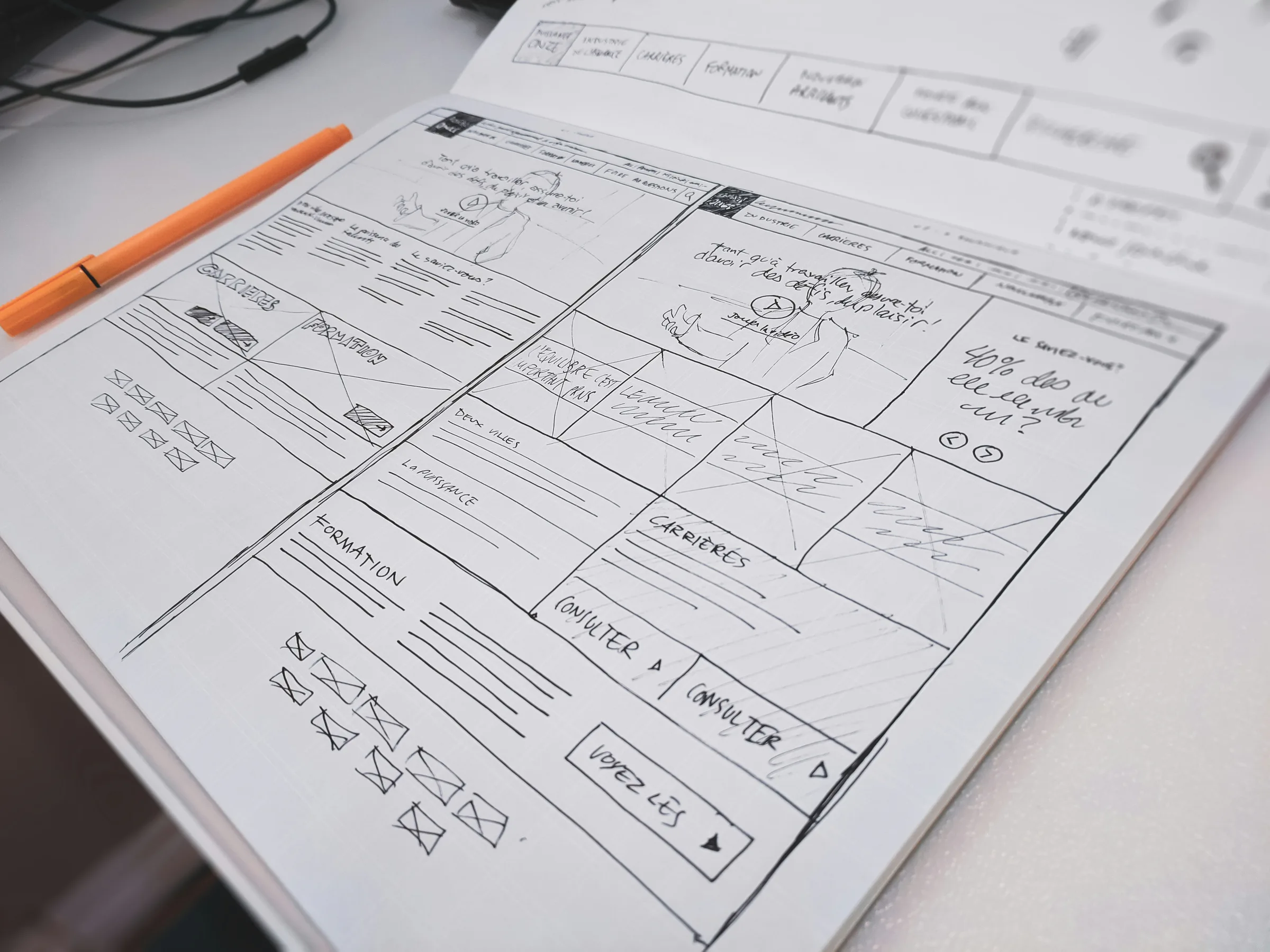 A website wireframe drawn by hand in a sketchbook, an orange pen beside it